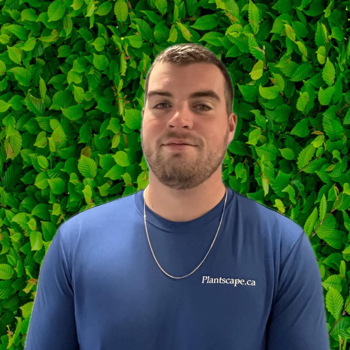 A person is smiling against a green leafy backdrop, wearing a blue shirt with "Plantscape.ca" text, and a necklace.